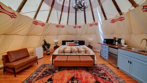 A cozy tented accommodation with a bed, sofa, and kitchenette.