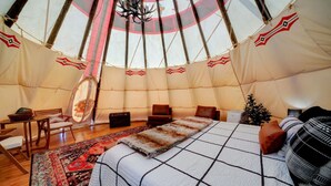 A cozy interior of a round tent with a bed, chairs, a small table, and a decorative mirror.