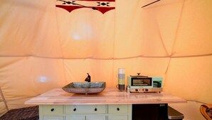 A tent interior with a table, a bowl, a kettle, and a portable stove.