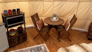 Un ambiente interior acogedor con una mesa redonda de madera, dos sillas de madera, un estante con cuencos de colores y un microondas sobre un soporte.