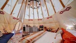 Interior acogedor de una yurta con una cama, una pequeña cocina y una mesa de comedor.
