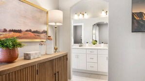 A modern bathroom with a wooden vanity, a large mirror, and a painting above the mirror. - 6 Bed 6 Bath Sleeps 22 w/4 Private Master Suites! (Hurricane)