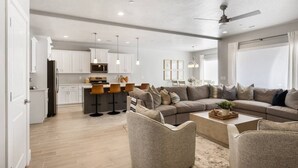 A modern living room with a sectional sofa, a coffee table, and a kitchen area with bar stools. - 6 Bed 6 Bath Sleeps 22 w/4 Private Master Suites! (Hurricane)