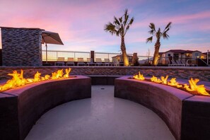 Een terras met zitgedeelte, vuurkorven en lounge fauteuils, omgeven door palmbomen en een stenen muur.
