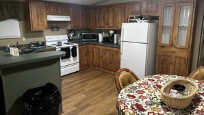 A kitchen with wooden cabinets, a white stove, a microwave, and a refrigerator. There is a dining table with a floral tablecloth and a basket.