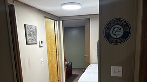 A hallway with a wooden floor, a white washing machine, a door with a sign, and a door leading to a room with a bed.