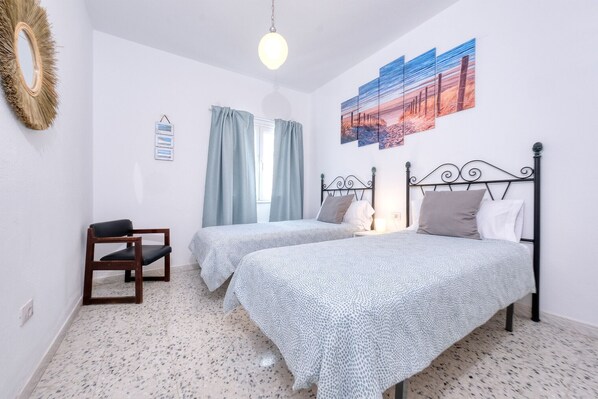 A bedroom with two beds, a wooden chair, a mirror, and a painting on the wall. - Casa Hespi - View to Famara Beach By LVH (Famara)