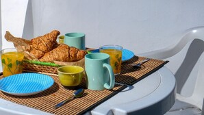 Disposição para o café da manhã com croissants, café e suco em um terraço com vista para uma paisagem montanhosa e edifícios modernos.