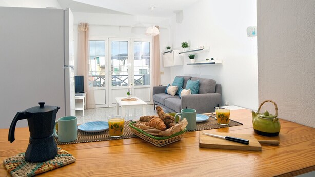 Sala moderna com sofá, mesa de centro e espaço para café da manhã, incluindo croissants, chaleira e bule.