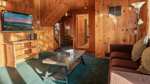 Ein Holzhütten-Interieur mit Fernseher, Holztisch, einer Couch und einer Treppe, die in einen anderen Raum führt.
