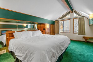 Un dormitorio con una cama grande, cabecera de madera, alfombra verde y una ventana con cortinas.