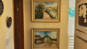 A hallway with two framed paintings on the wall, a wooden door, and a wooden floor. - Large house in a gated community, 3 bedrooms, 5 bathrooms and a large backyard. (Atibaia)