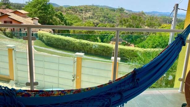 A hammock on a balcony with a view of a green landscape and distant hills. - Large house in a gated community, 3 bedrooms, 5 bathrooms and a large backyard. (Atibaia)