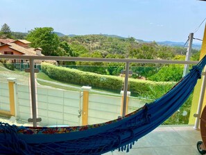 Una hamaca en un balcón con vistas a un paisaje verde y colinas lejanas.
