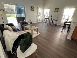 Relax in this open-plan living space with a dining area and seating space, featuring a coffee table and a large window with a view of the outdoors.