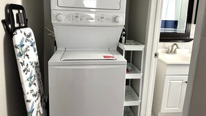 A compact laundry area with a washing machine and dryer, a small sink, and a mirror above the sink. - A Beautiful Storey - Quiet Condo minutes from Midland Memorial (MIDLAND)