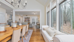 Une cuisine spacieuse avec un plancher en bois, un coin repas doté d’une grande table et de chaises, et un coin salon confortable avec un canapé blanc et des coussins.