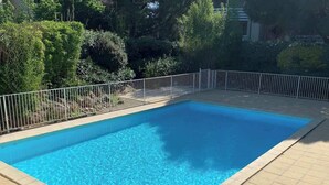 Una piscina rectangular con agua azul cristalina, rodeada por un borde de baldosas y una cerca metálica.