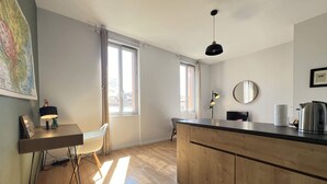 Una cocina moderna con armarios de madera, encimera negra y una lámpara colgante. Se ve una ventana que proporciona luz natural y un mapa en la pared.