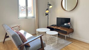 Una sala de estar moderna con un sofá, un televisor, una lámpara y un espejo redondo.