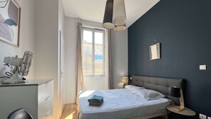 Un dormitorio con cama, mesita de noche, silla y escritorio con lámpara.