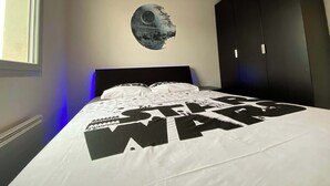 Un dormitorio con una colcha temática de Star Wars, un adorno mural circular y un armario oscuro.