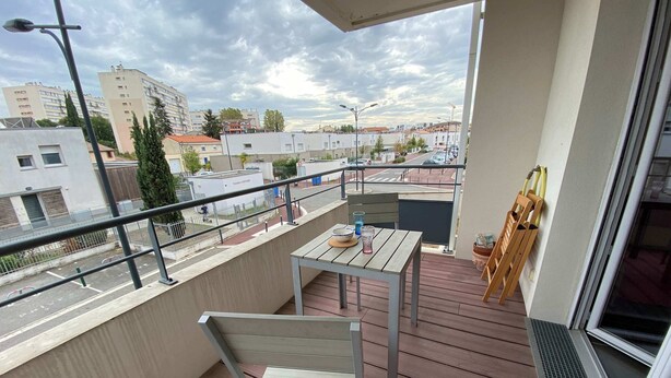 Un balcón con mesa y silla, vista del paisaje urbano, y barandilla.