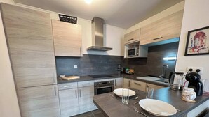 Una cocina moderna con armarios de madera clara, encimera oscura y electrodomésticos de acero inoxidable.