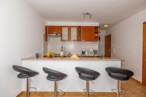 Una cocina con armarios de madera, encimera blanca y tres taburetes negros.