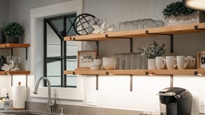 Ett modernt kök med trähyllor där glas och skålar står, en kaffebryggare och en diskho med blandare.