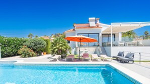 A modern pool area with lounge chairs and an umbrella, surrounded by lush greenery and a clear blue sky. - CostaBlancaDreams - Villa Hermosa in Calpe (Calpe)