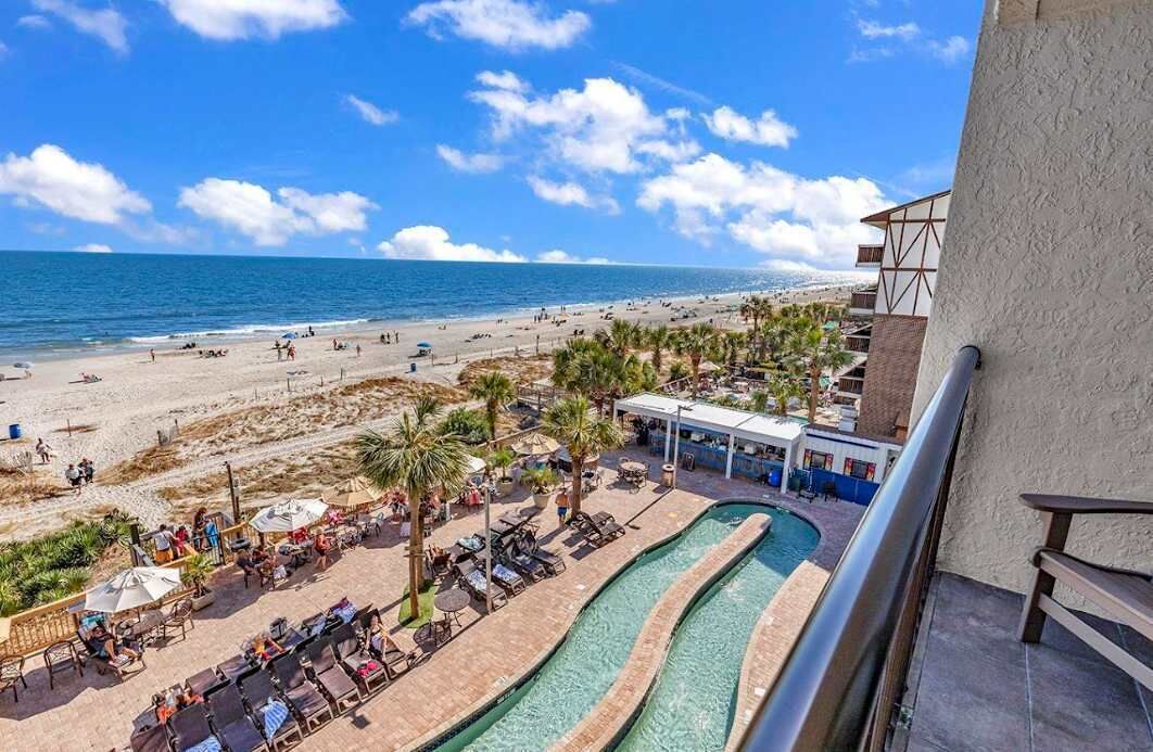 A beach resort with a pool, lounge chairs, and a view of the ocean.