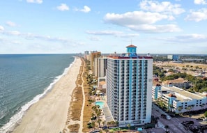 Un hotel costero con vista a la playa, varios pisos y una torre destacada.