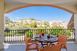 A balcony with a round table and orange chairs, overlooking a residential area with buildings and greenery.