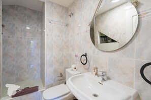 A bathroom with a shower, toilet, sink, and a round mirror.