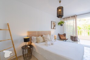 A neatly arranged bedroom with a large bed, bedside tables, a hanging plant, and a view of the outdoors.