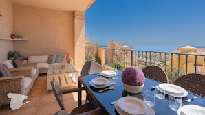 Un balcon avec une table à manger pour quatre personnes, des meubles en osier et une vue dégagée sur la mer.