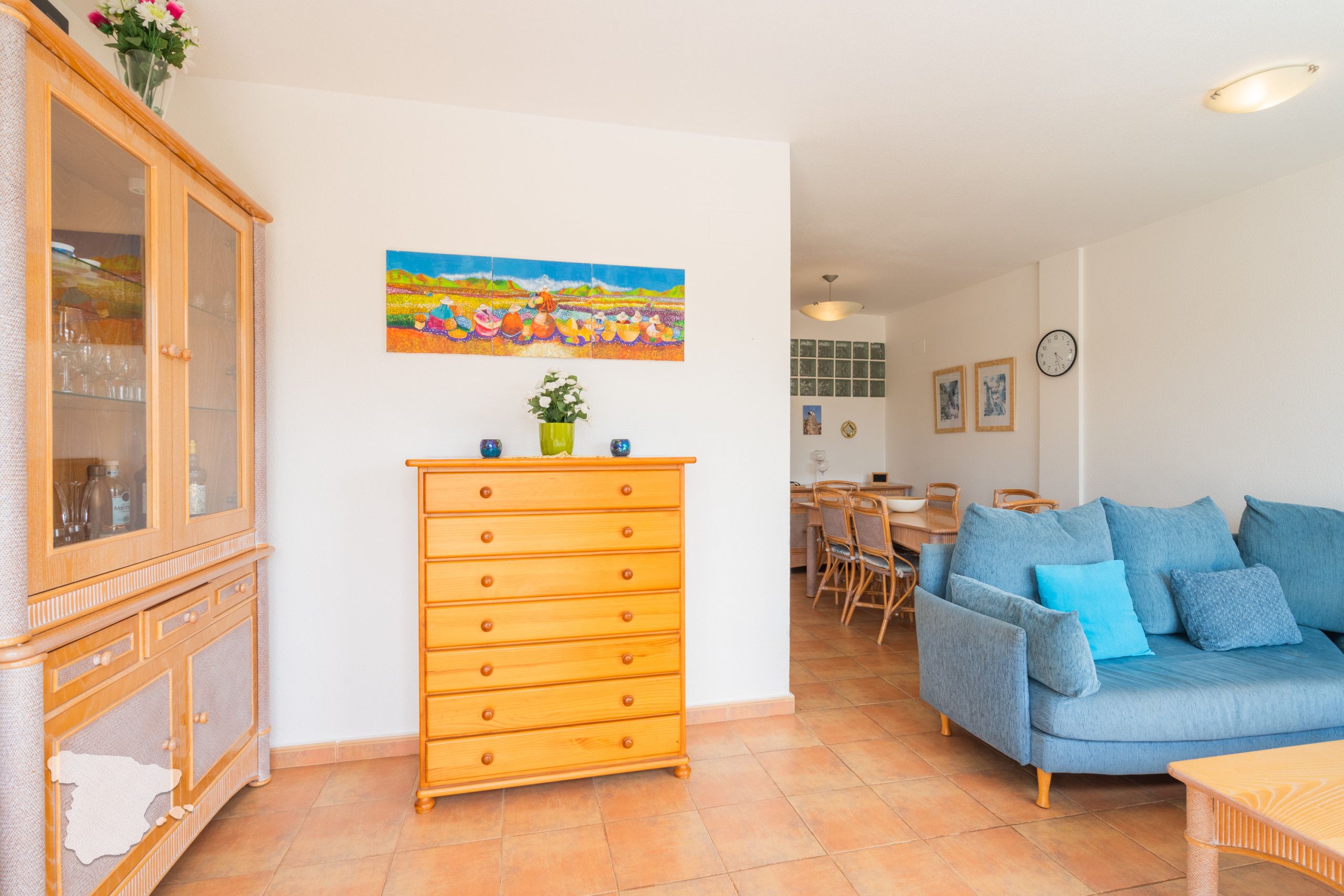 Ein Wohnzimmer mit einem Holzkabinett, einem blauen Sofa, einem Essbereich und einem Gemälde an der Wand.