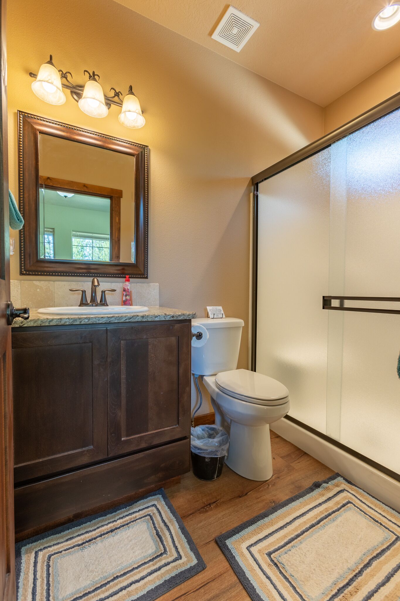 Un baño con tocador de madera, lavamanos, inodoro y zona de ducha.
