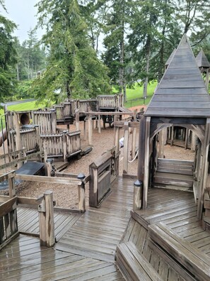 A wooden play structure with multiple levels and slides, surrounded by trees. - Coastal Retreat on Lake, mins to Ocean, Casino, Restaurants, Shopping (Neotsu)