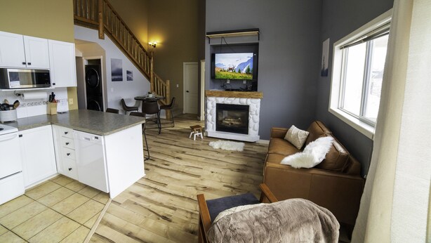 Ein geräumiger Wohnbereich mit Kamin, einem darüber montierten Fernseher und einer gemütlichen Sitzecke mit braunem Sofa.