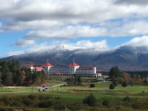 Un grande edificio con tetti rossi, circondato da un campo da golf e montagne sullo sfondo.