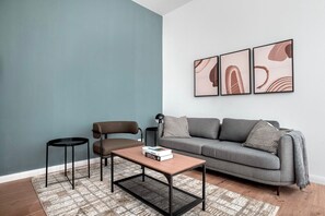 A living room with a grey sofa, a brown chair, a small table with books, and a patterned rug.