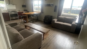 Una sala de estar moderna con un sofá, una mesa de centro de madera y una zona de cocina con estufa y taburetes de bar.