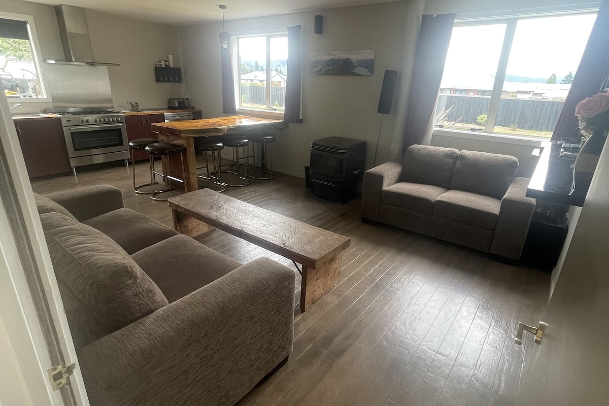 Uma sala de estar moderna com um sofá, uma mesa de centro de madeira e uma cozinha com fogão e banquetas.