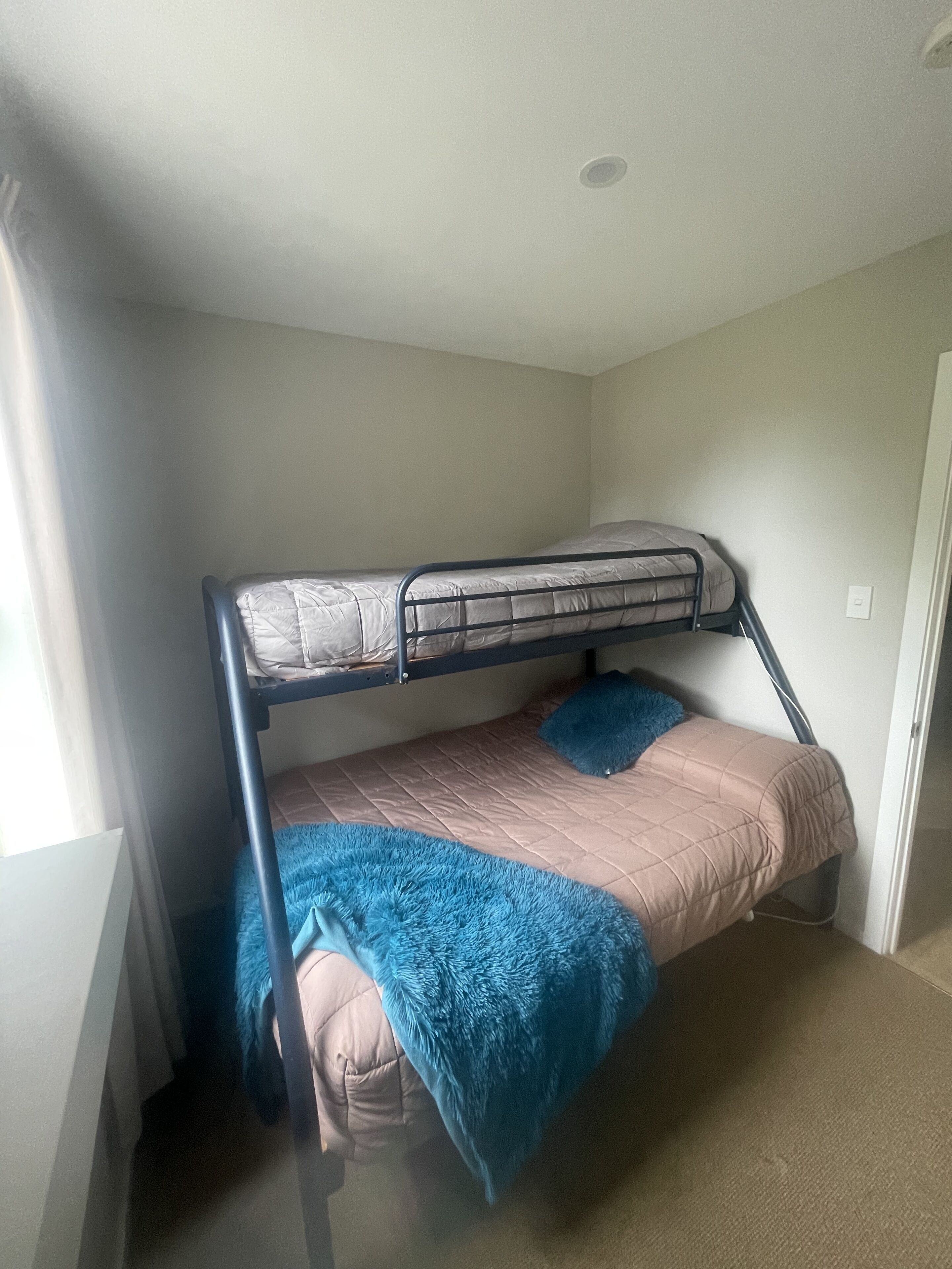 A bunk bed with a blue blanket and a pink bedspread in a room with beige walls and a white ceiling.