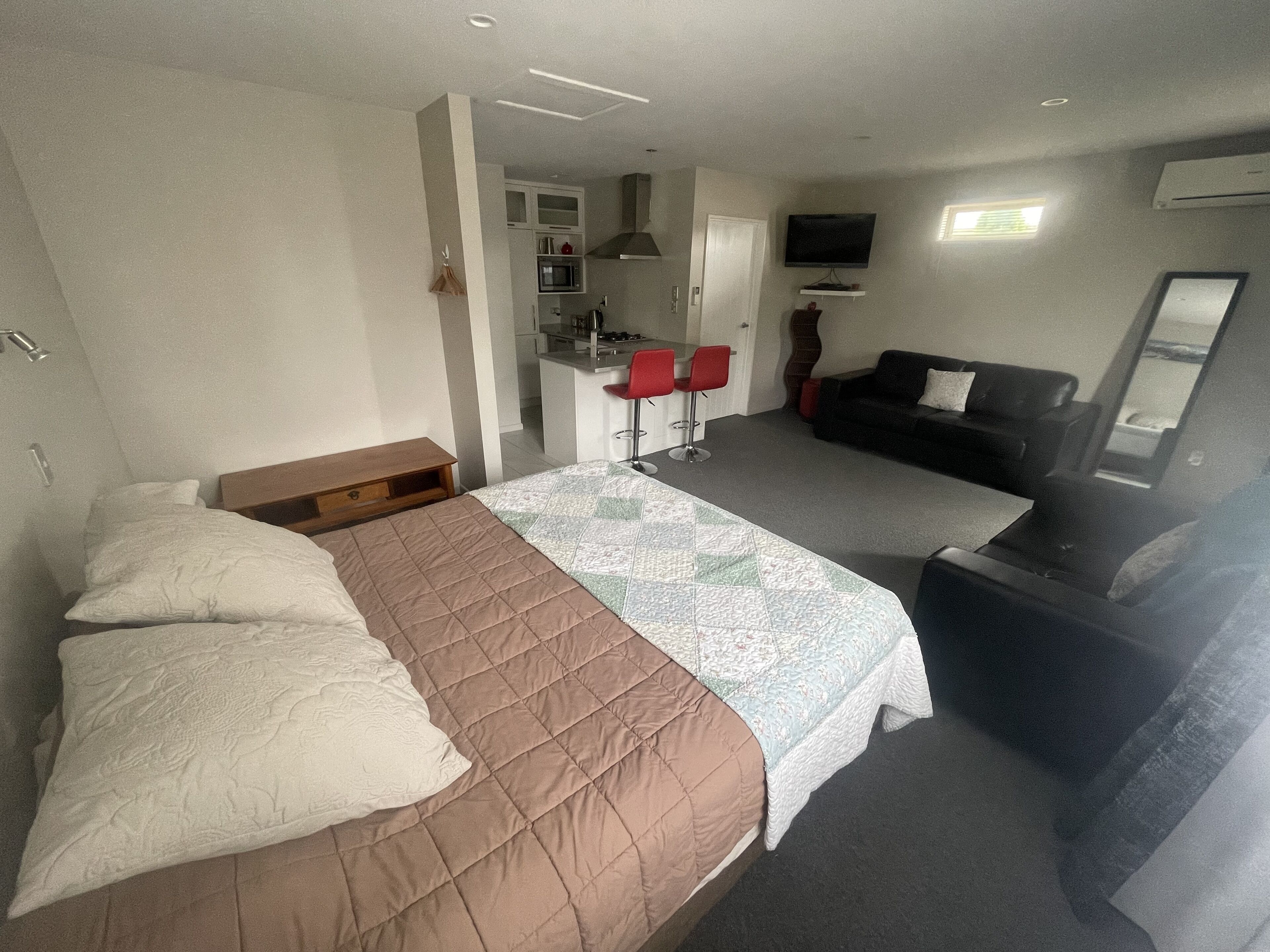 Ein Hotelzimmer mit Bett, Sofa, Fernseher, einer kleinen Küchenzeile und einem Badezimmer.