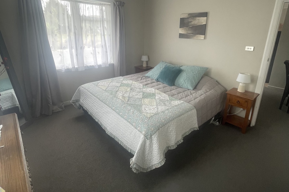 Quarto com cama, mesa de cabeceira, abajur e um quadro na parede.