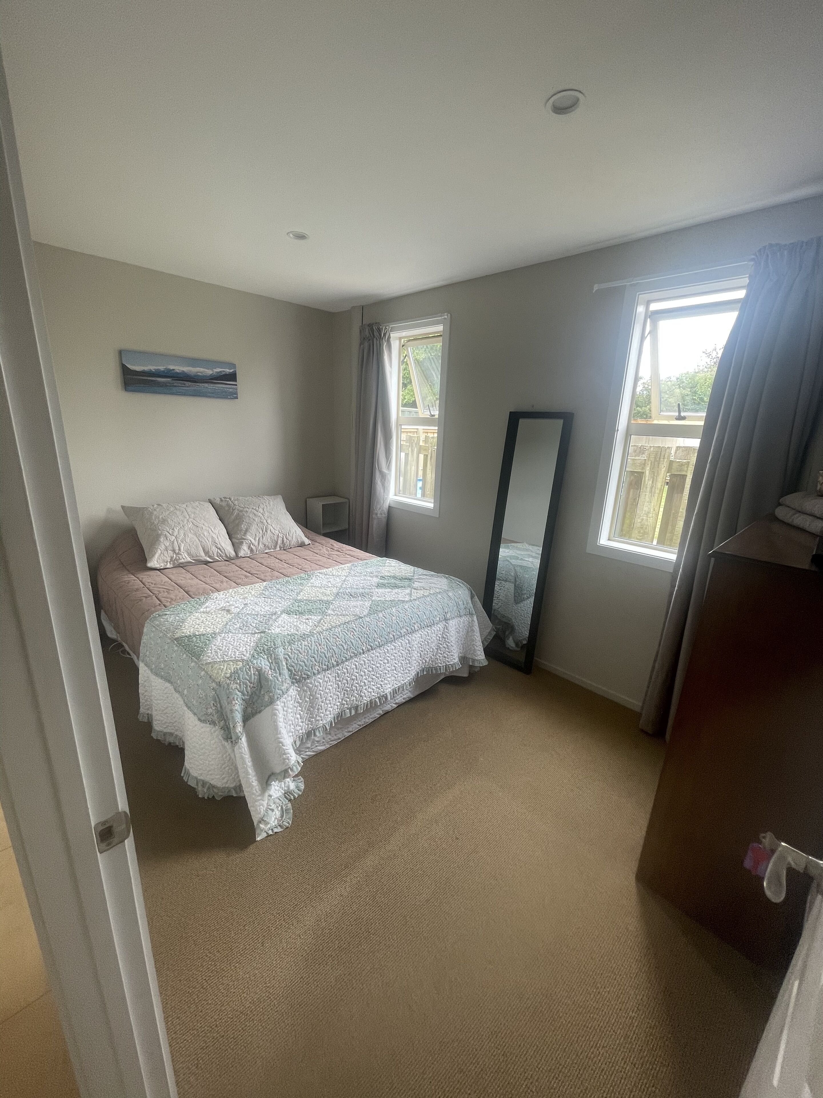 A bedroom with a bed, a bedside table, a dresser, a window with curtains, and a painting on the wall.