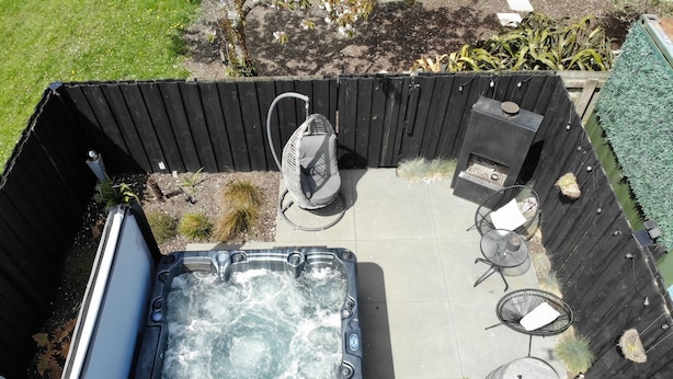 Un jacuzzi rodeado por una terraza de madera, con un área de estar y un pequeño hogar para fuego.